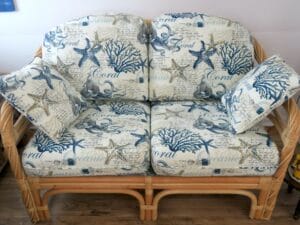 Rattan love seat with all loose pleated cushions for a seasonal cottage on Cape Cod | Upholstered in an indoor-outdoor beach theme fabric | Upholstered by Cape Cod Upholstery Shop | Located in South Dennis, MA 02660